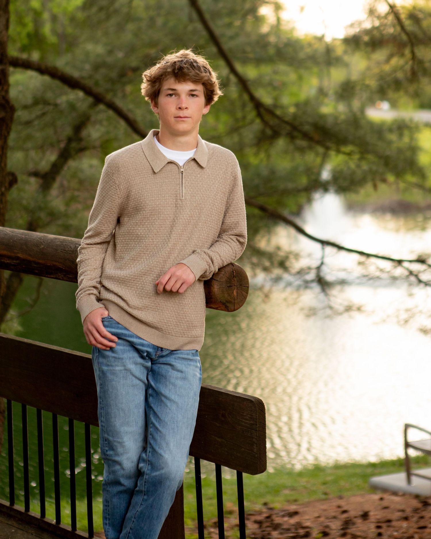 Person in beige sweater leans on railing with lake view in background.