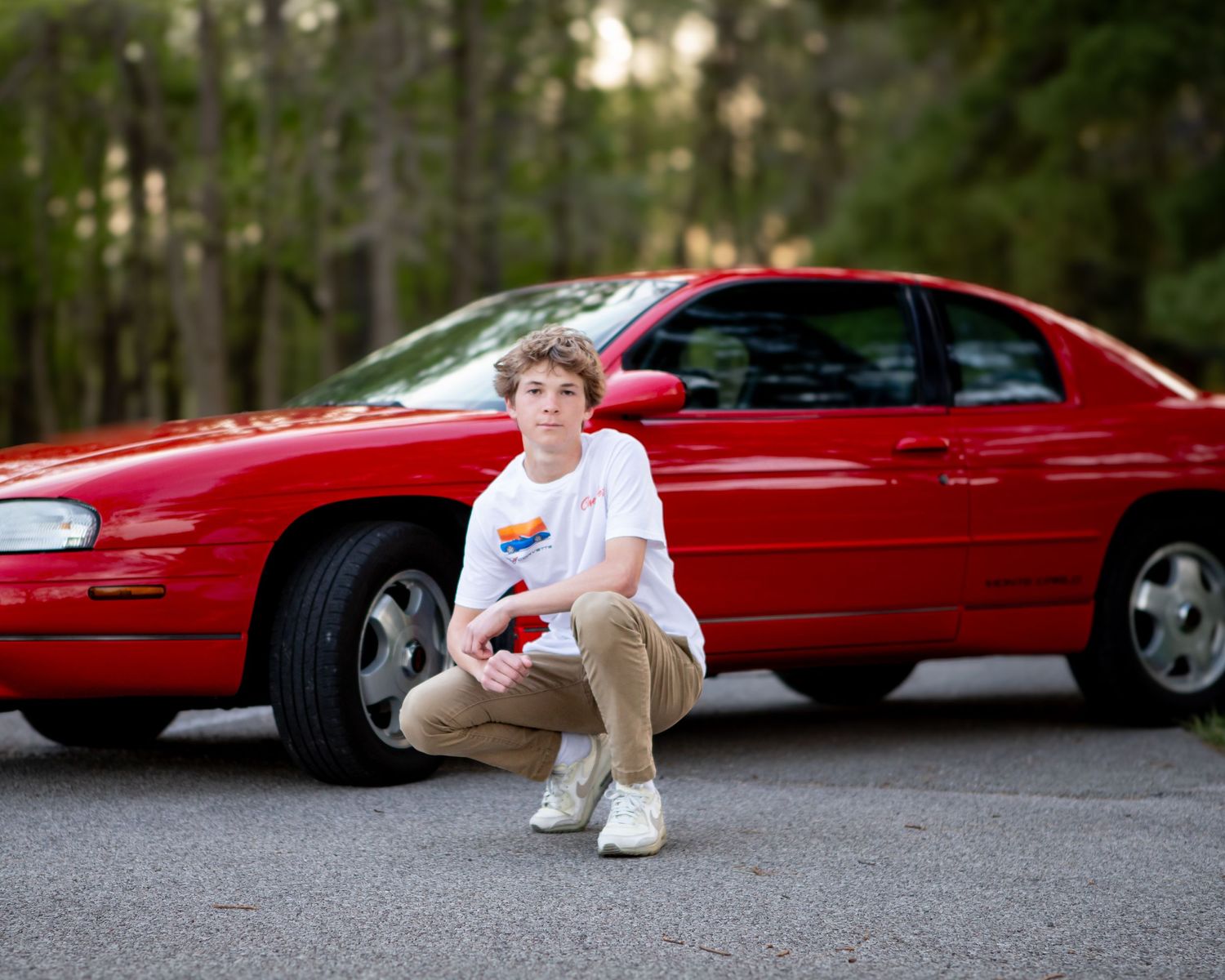 Multiple angles of someone lounging against a shiny red convertible car parked on a forest road.