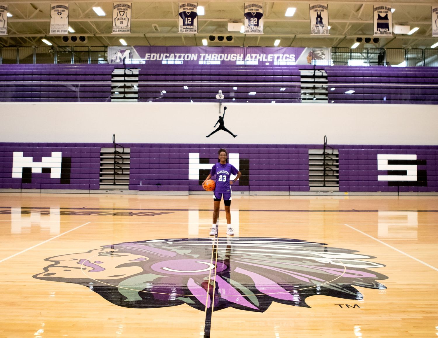 Wide view of an indoor basketball court with purple team branding and decorations.