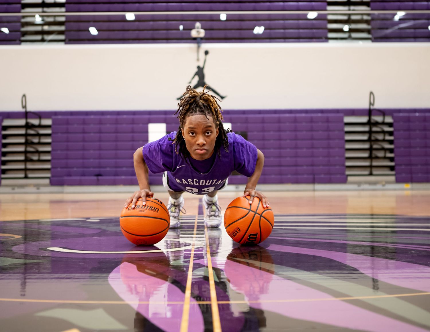 Basketball player in purple uniform practicing dribbling drills in a gymnasium.