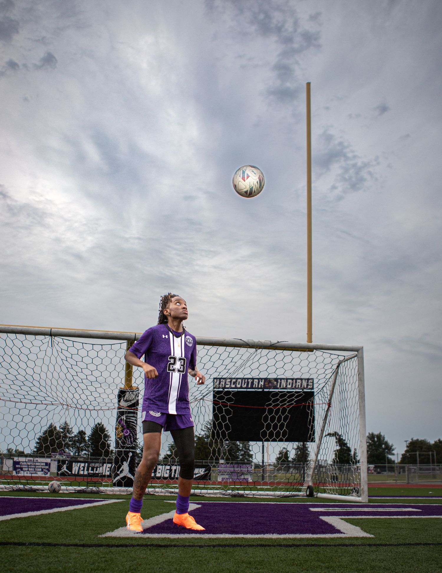 Soccer player in purple uniform practicing goal kicks on a field under cloudy skies.