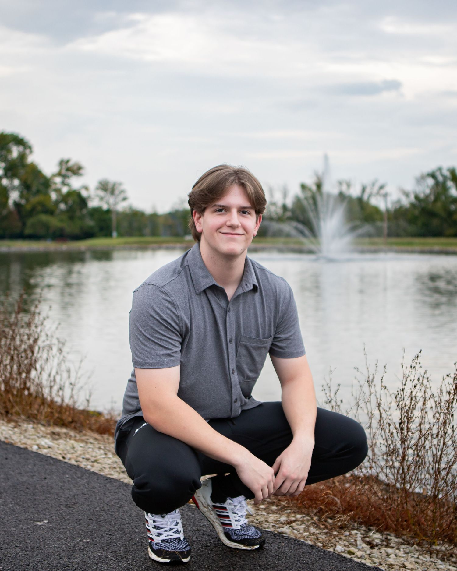 Outdoor portrait session by a lake with fountain featuring casual poses in grey clothing.