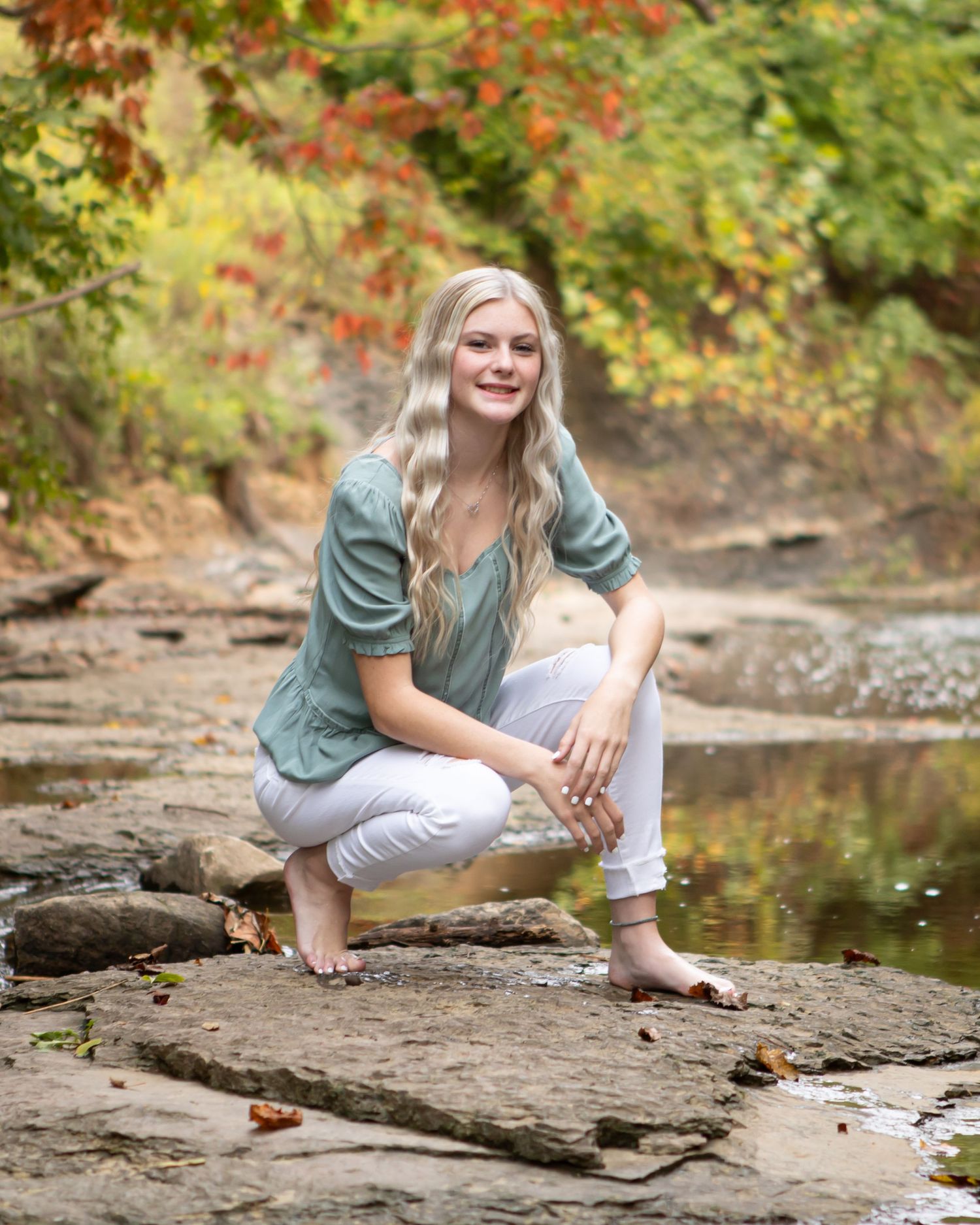 Outdoor portrait on rocks by stream with autumn foliage in background.