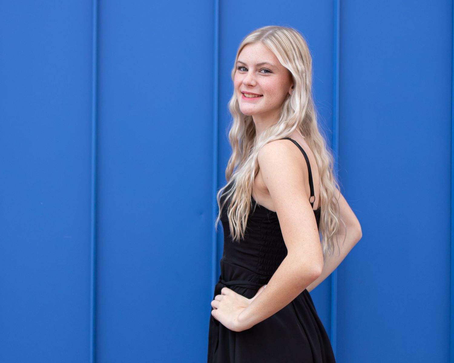 Portrait against bright blue wall background wearing black dress.
