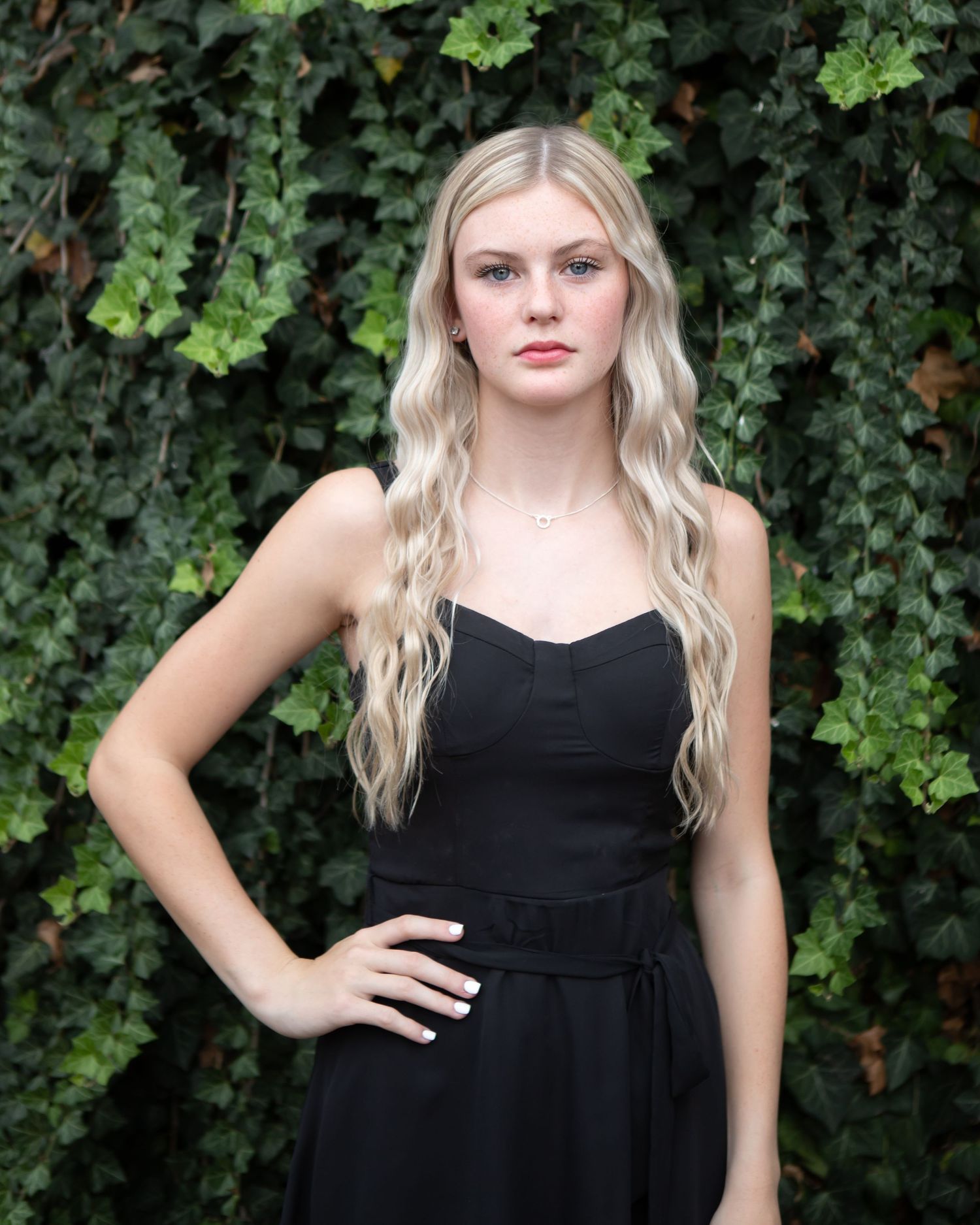 Portrait session in front of ivy covered wall wearing black dress.