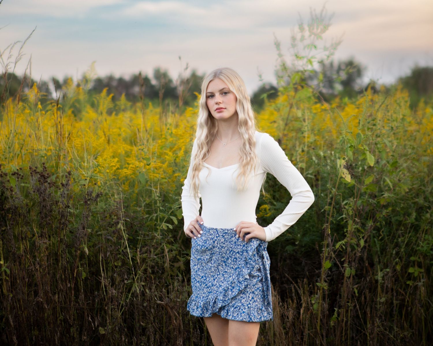 Outdoor portrait in white top and floral shorts among wildflowers at sunset.
