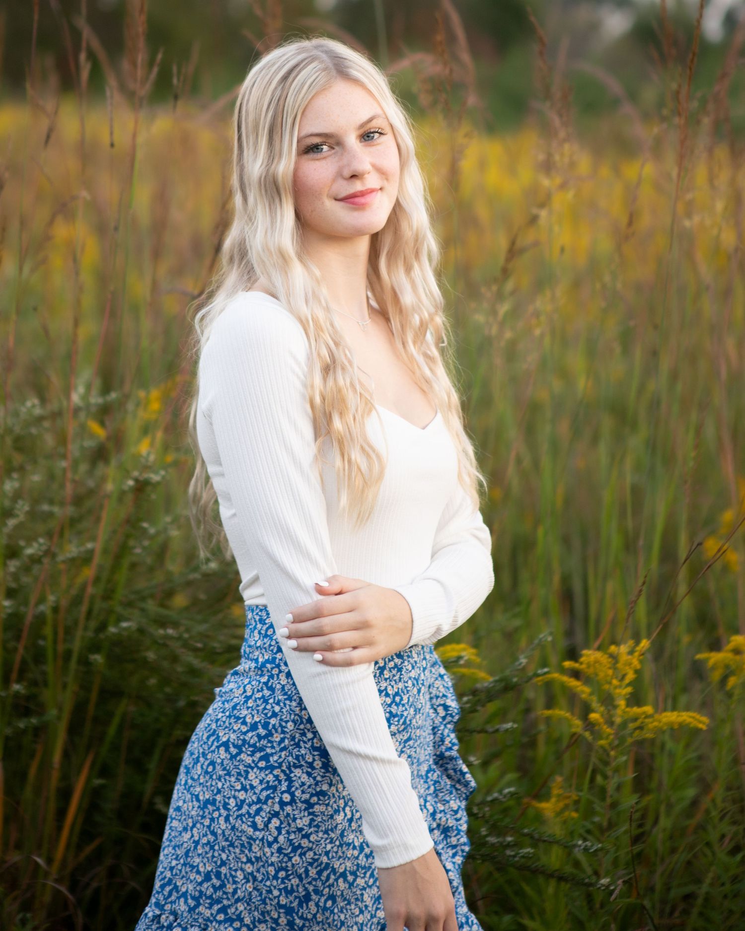 Portrait session in white top and floral skirt surrounded by golden wildflowers.