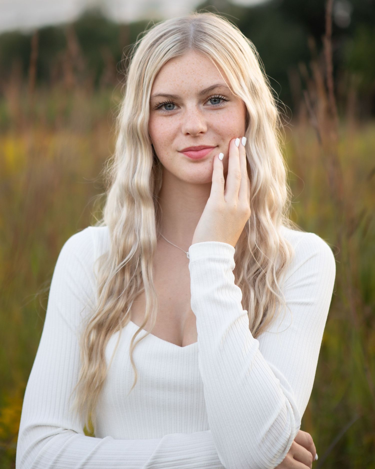 Portrait series in a natural field setting with white sweater and soft expressions.