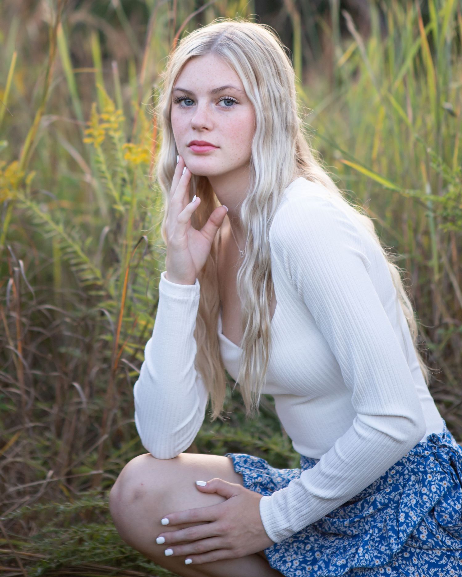 Outdoor portrait poses with white sweater and floral blue skirt in tall grass.
