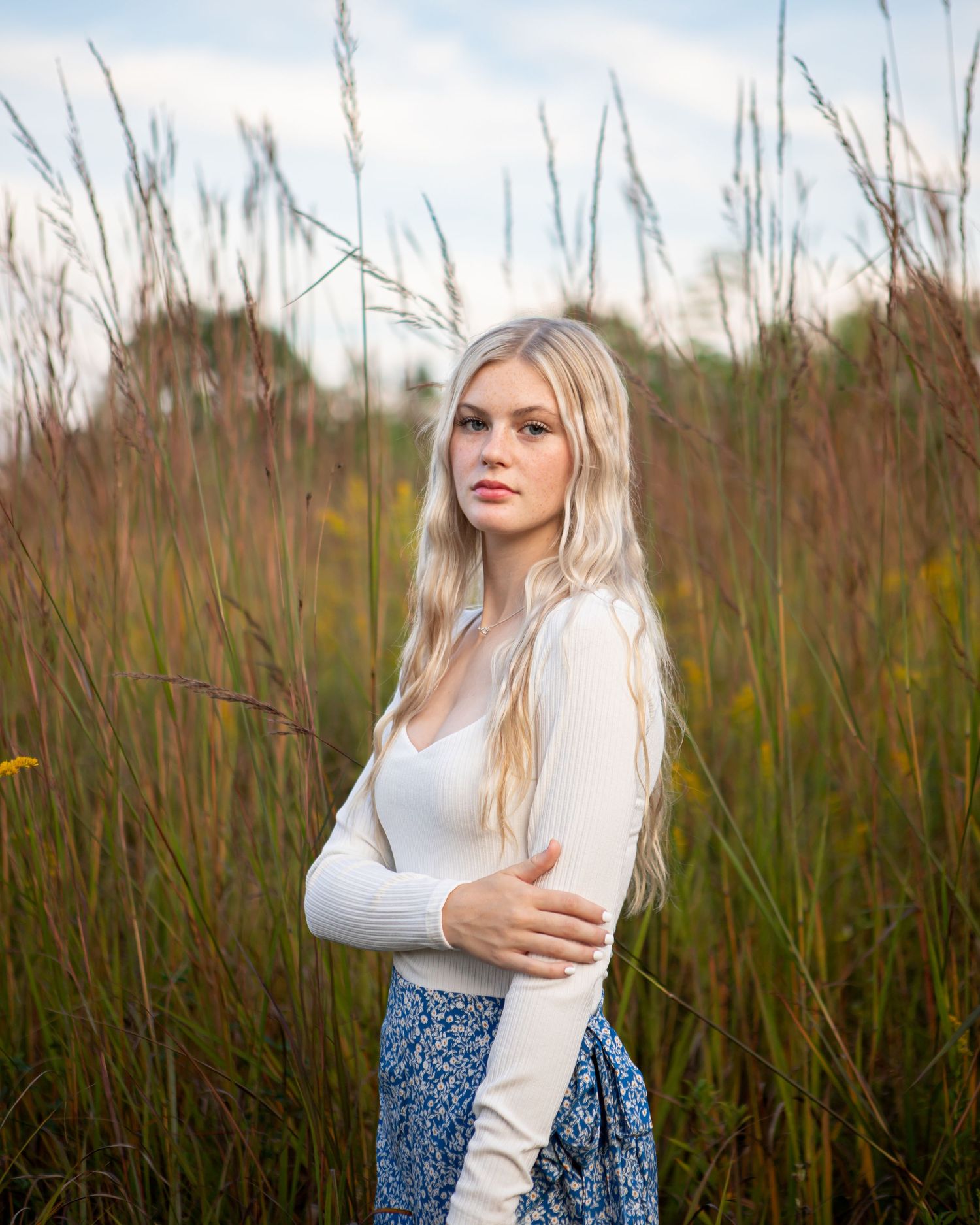 Artistic portrait sequence in tall grass field with white sweater and blue skirt.