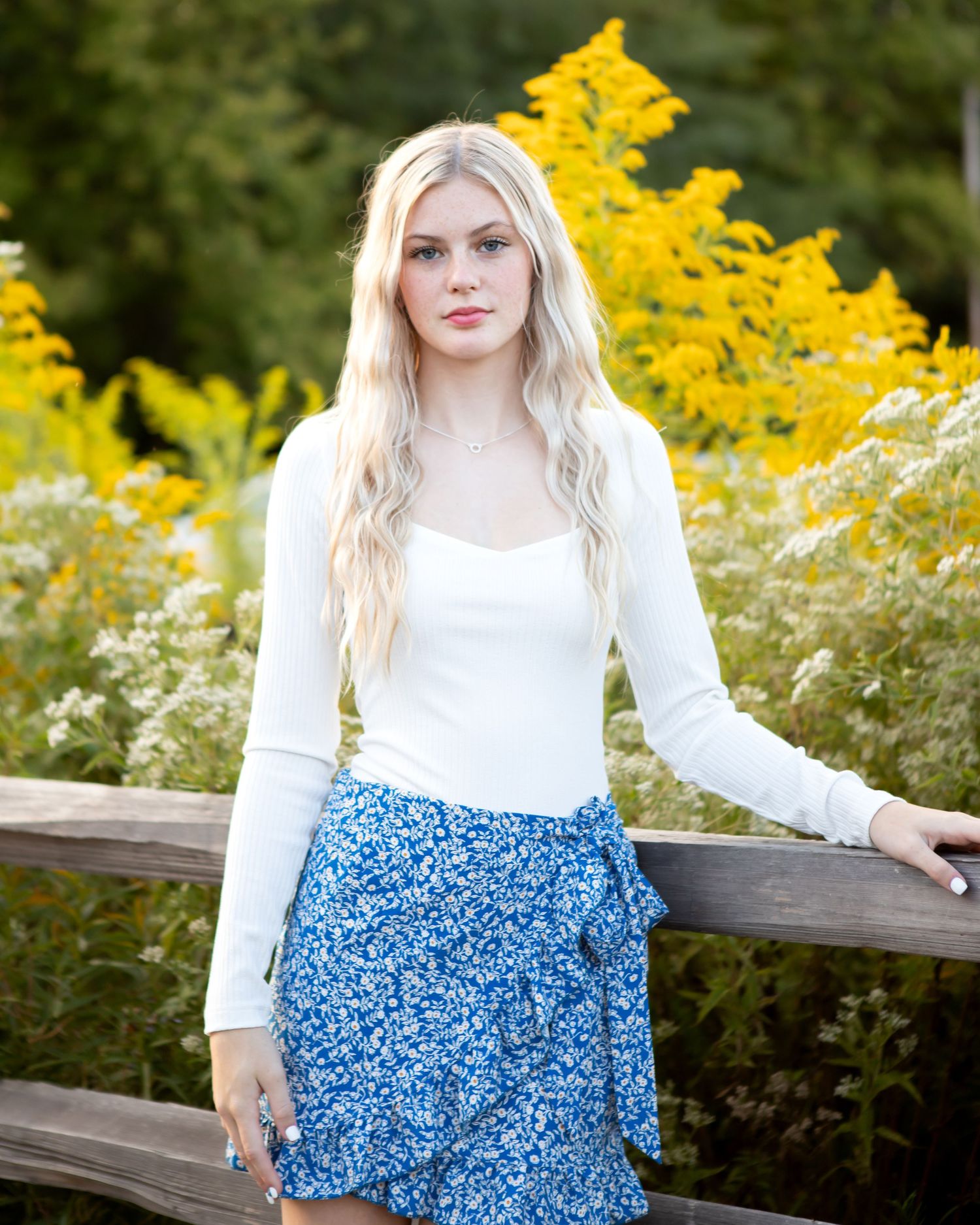 Portrait series against yellow wildflowers wearing white top and blue floral skirt.