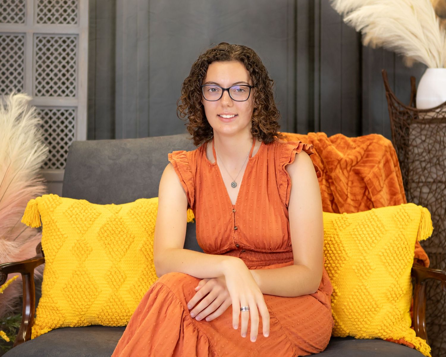 Indoor portraits on couch with yellow pillows wearing orange dress.