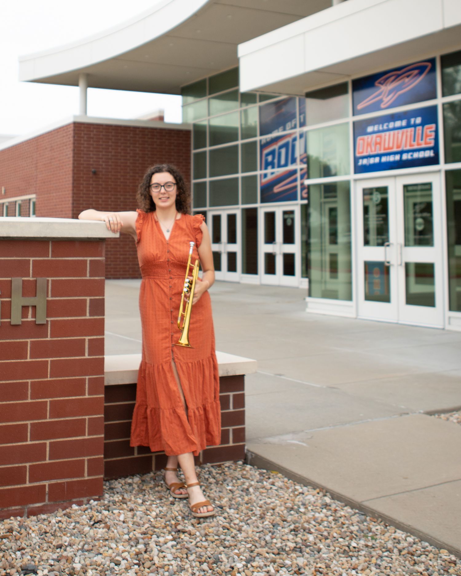 Outdoor portraits in orange dress near modern brick building entrance.