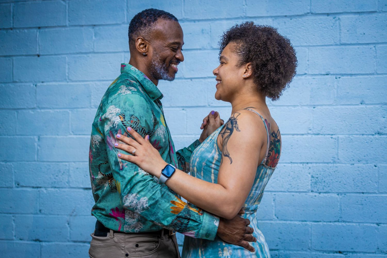 Couple in matching teal outfits share joyful moment against blue wall.