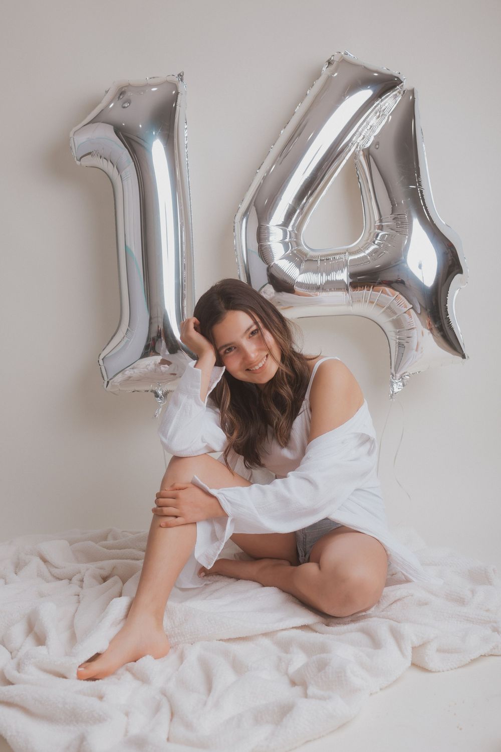 Casual birthday photo shoot with silver number balloons against white backdrop.