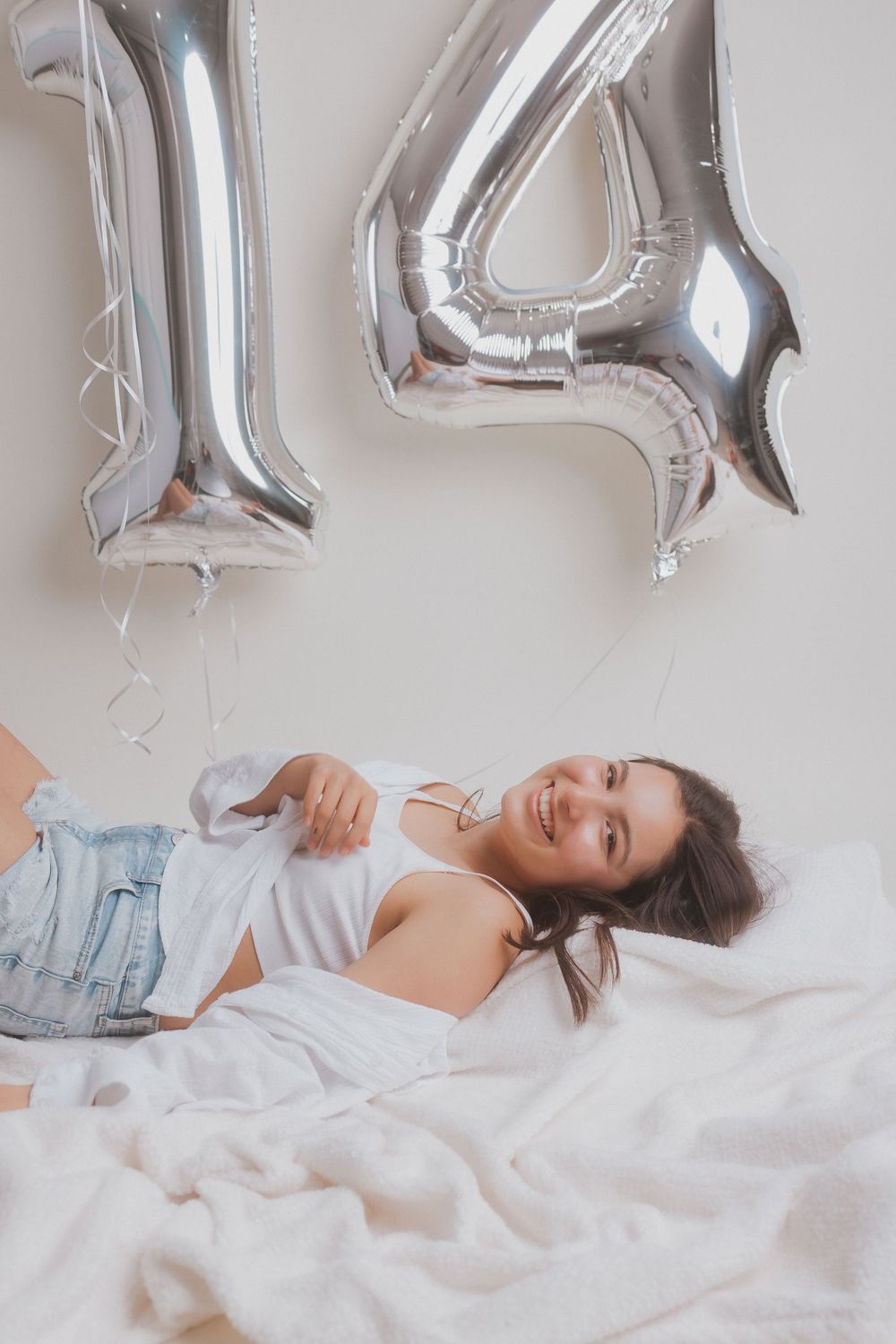 Lifestyle portrait with silver number balloons and casual outfit on white bedding.