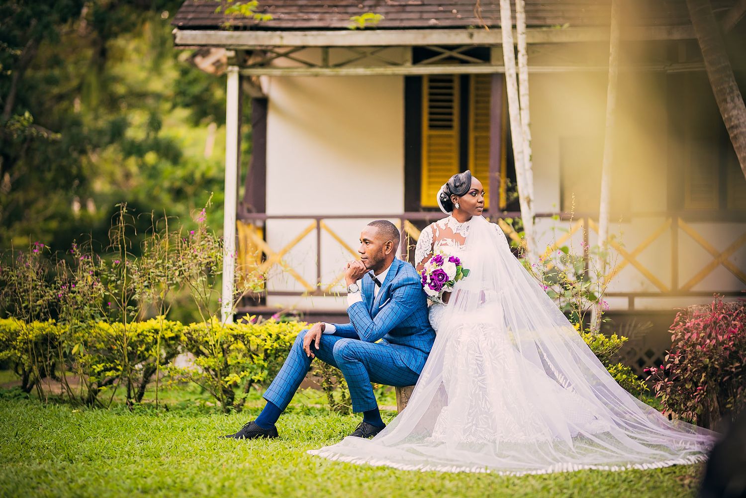 Wedding portrait of couple relaxing on porch of rustic house surrounded by garden.