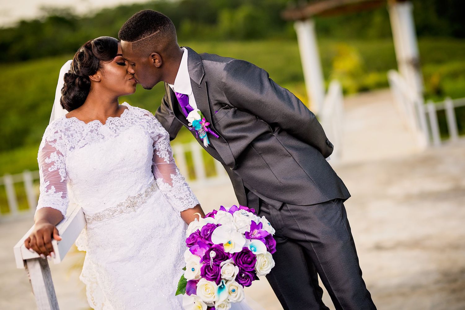Joyful wedding moment captured with purple floral bouquet and elegant white lace dress.