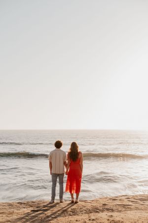 Silhouette of couple standing together watching sunset over ocean waves.