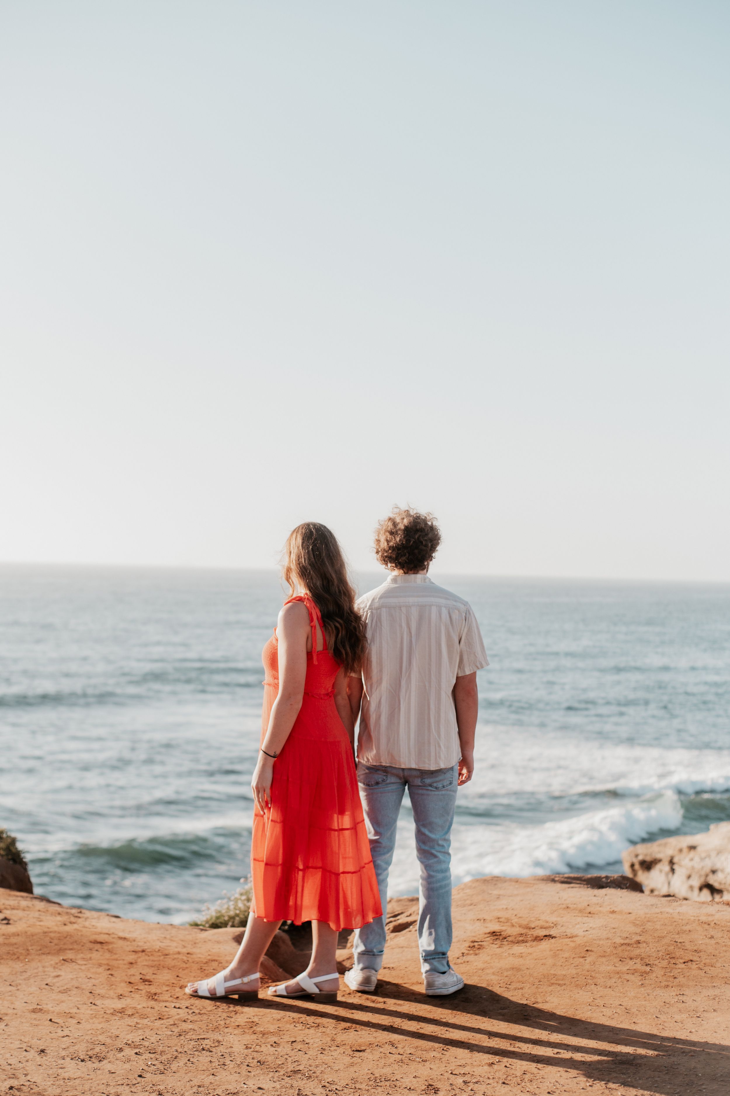 Couple sitting together enjoying ocean view on rocky coastal cliff.