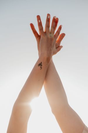Hands reaching up against bright sky showing small matching tattoos.