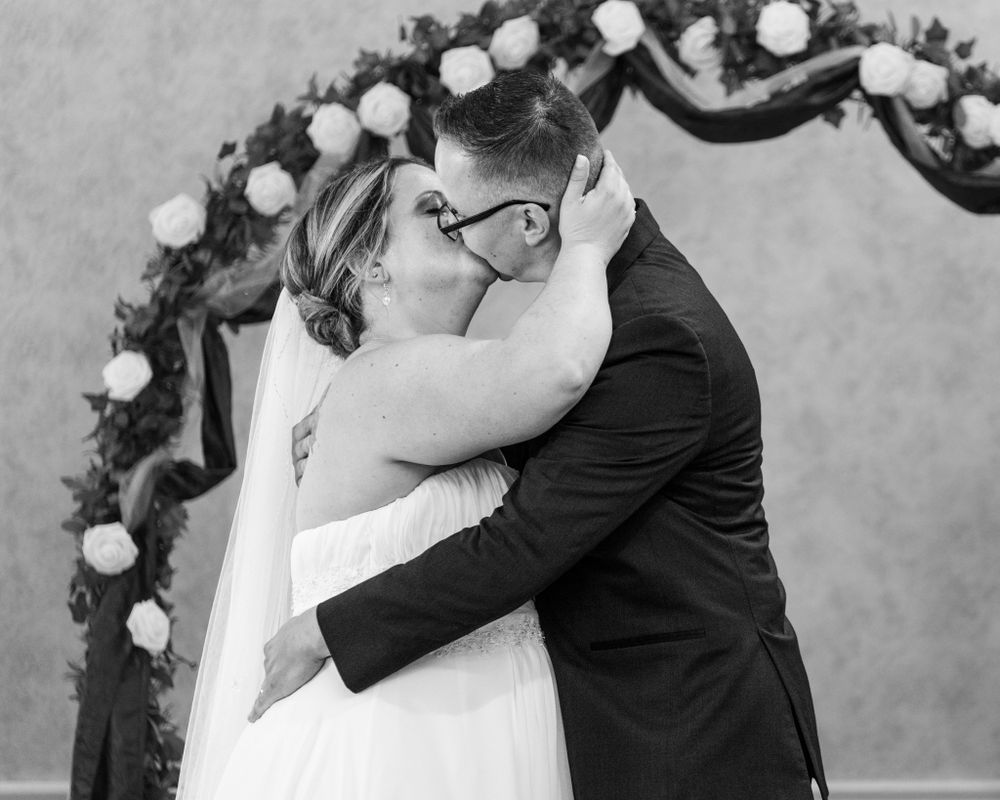A couple shares a romantic kiss under a floral arch during their wedding ceremony.