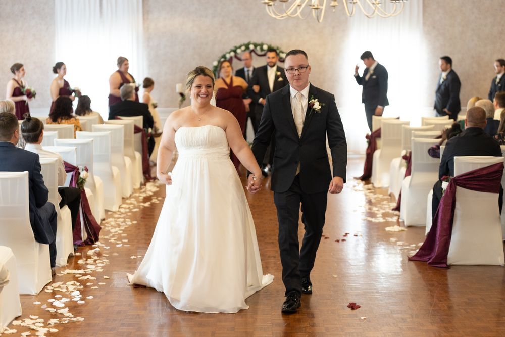 A couple walks down the aisle after their wedding ceremony with rose petals scattered on the floor.