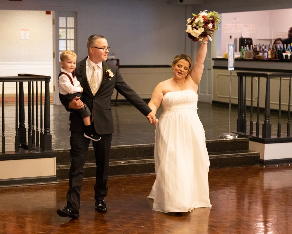 A wedding couple exits their ceremony venue on a wood floor stage.
