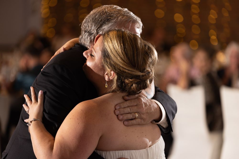A couple embraces during a romantic dance at their wedding reception with bokeh lights in background.