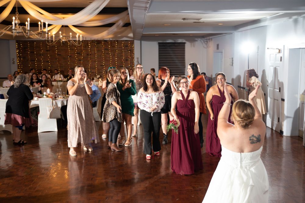 Wedding guests gather for the bouquet toss in a decorated reception venue.