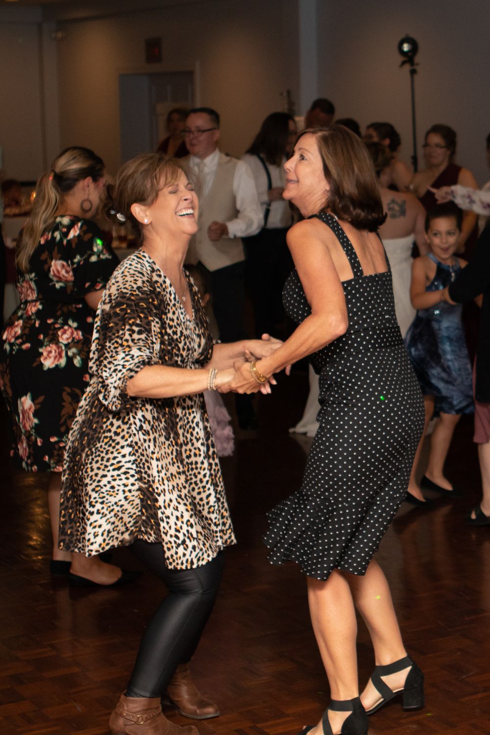 Two guests in patterned dresses share a joyful dance on the reception floor.