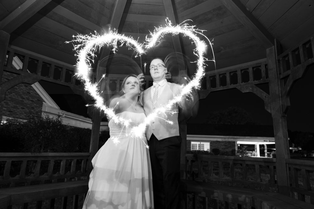A couple poses with sparklers creating a heart shape at their nighttime wedding.