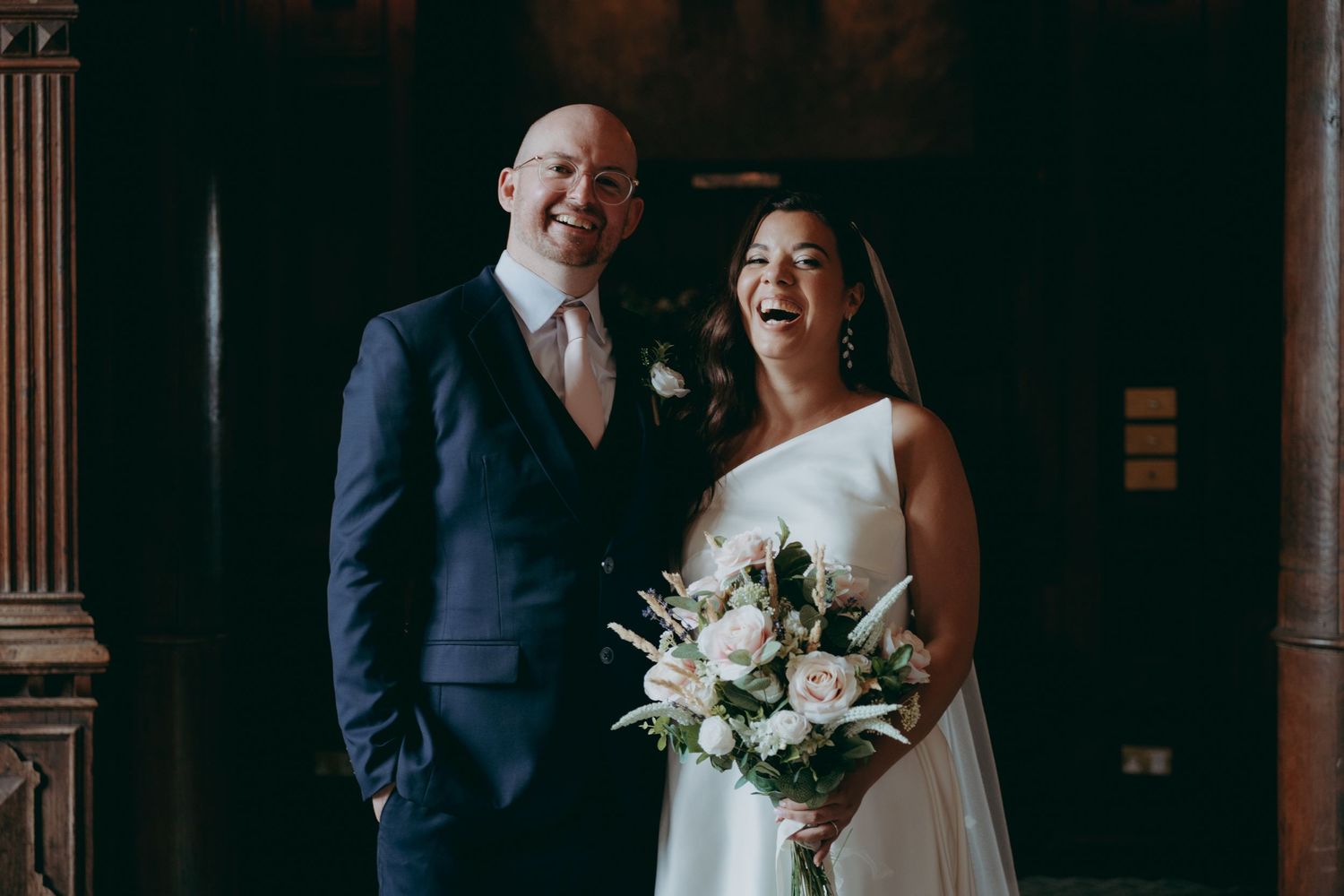 Wedding couple posing playfully in the rain with umbrella by rustic wooden barn. Shortmead House