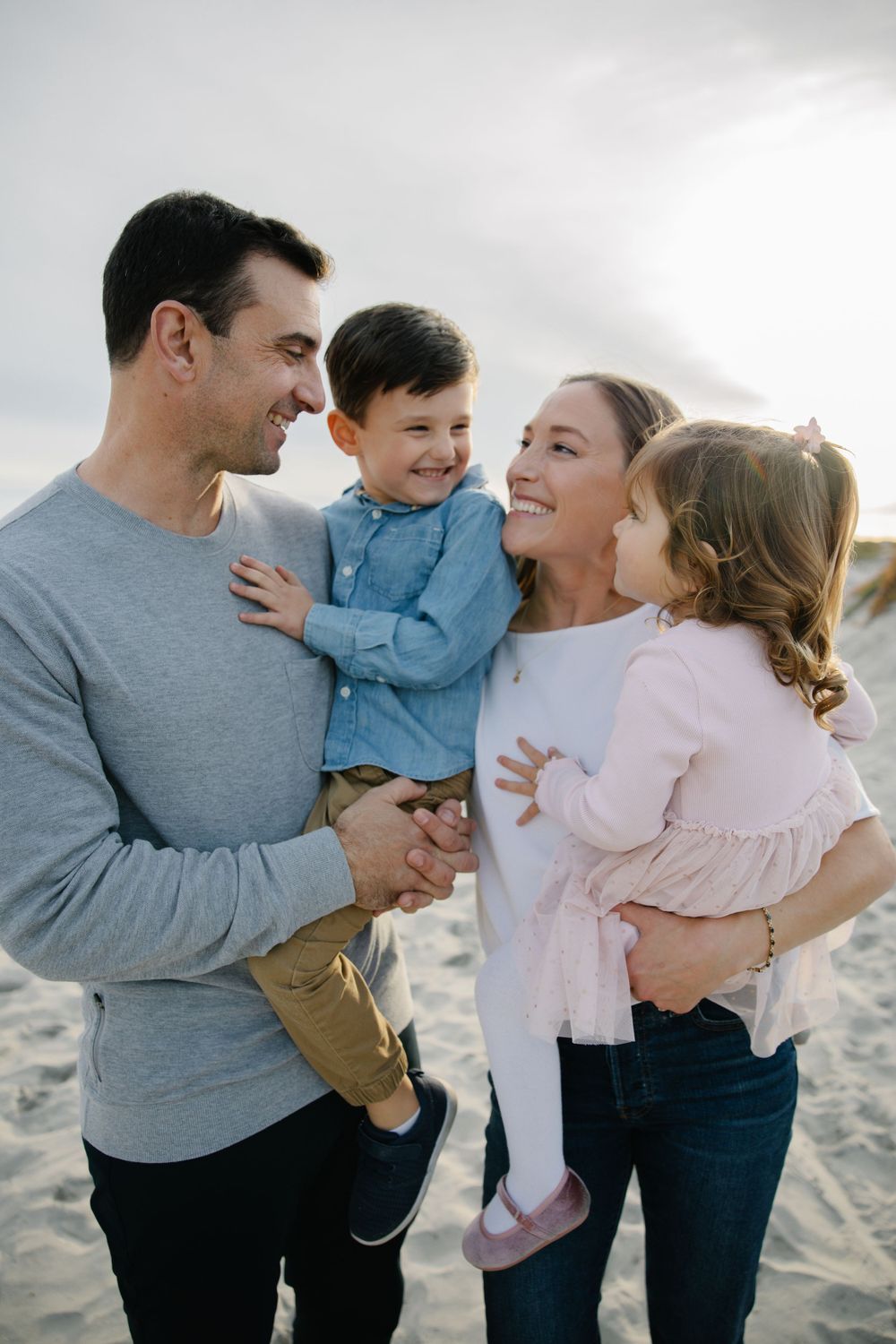 Happy family of four sharing warm embrace on sandy beach.