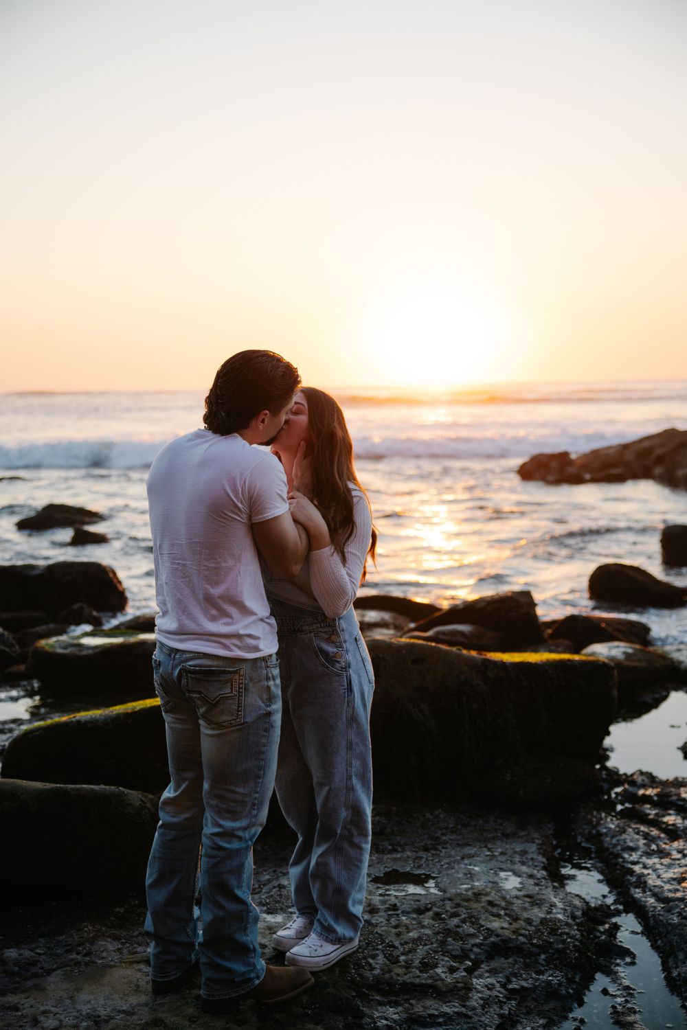 Couple sharing intimate moment on rocky beach at sunset.