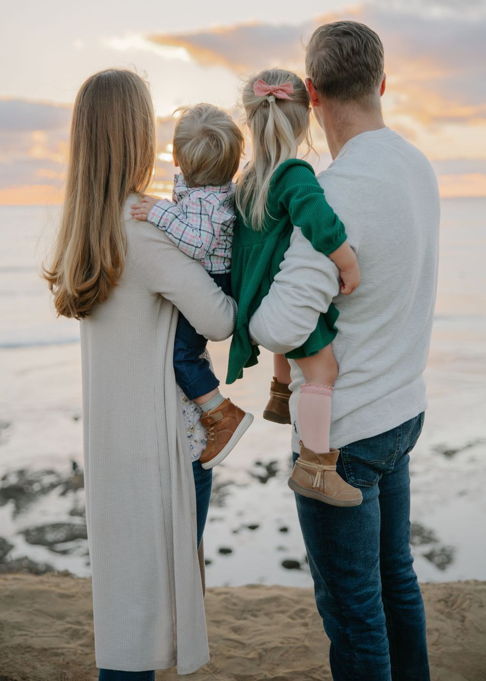 Family standing together watching sunset on beach with children.