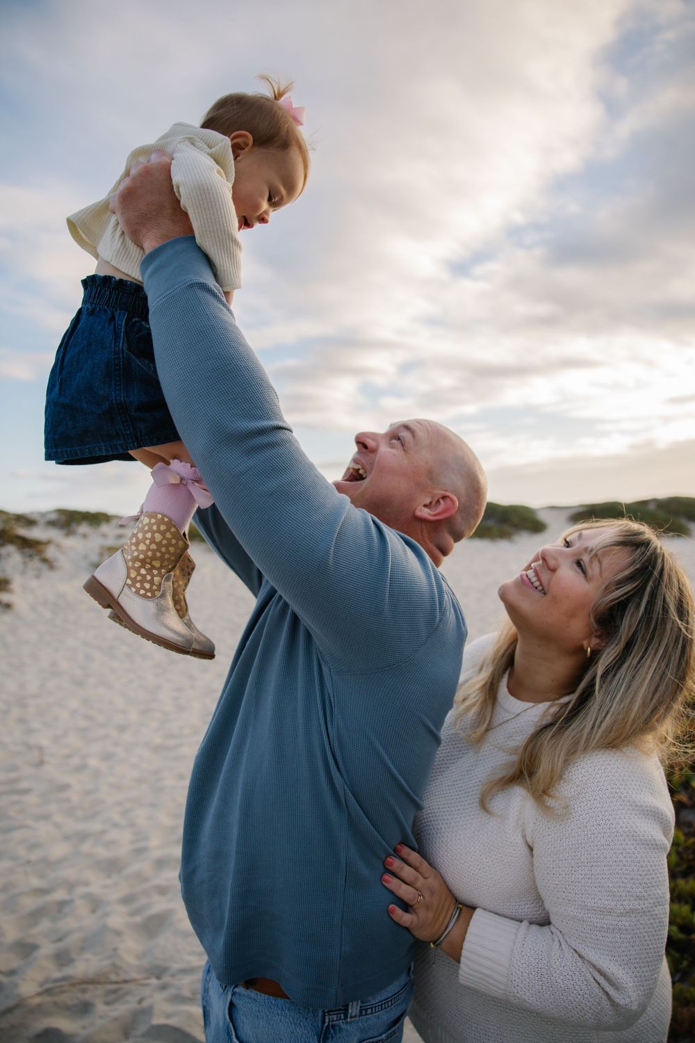 Parents playing with baby on sandy beach at sunset.