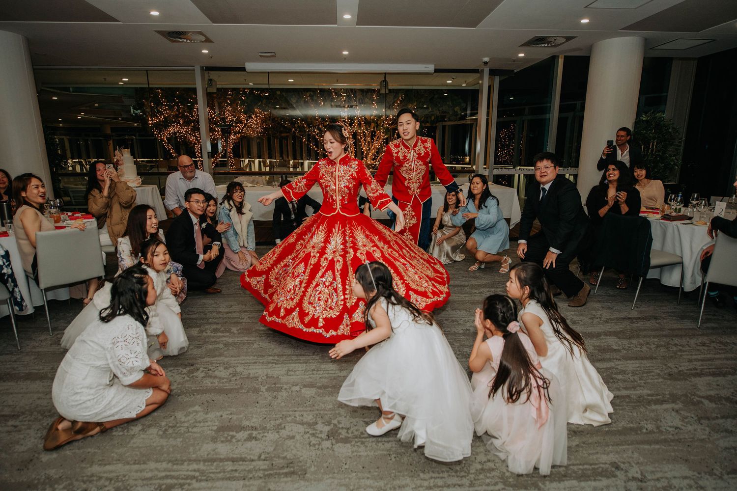 Wedding reception dance with couple in red traditional Chinese attire surrounded by guests.