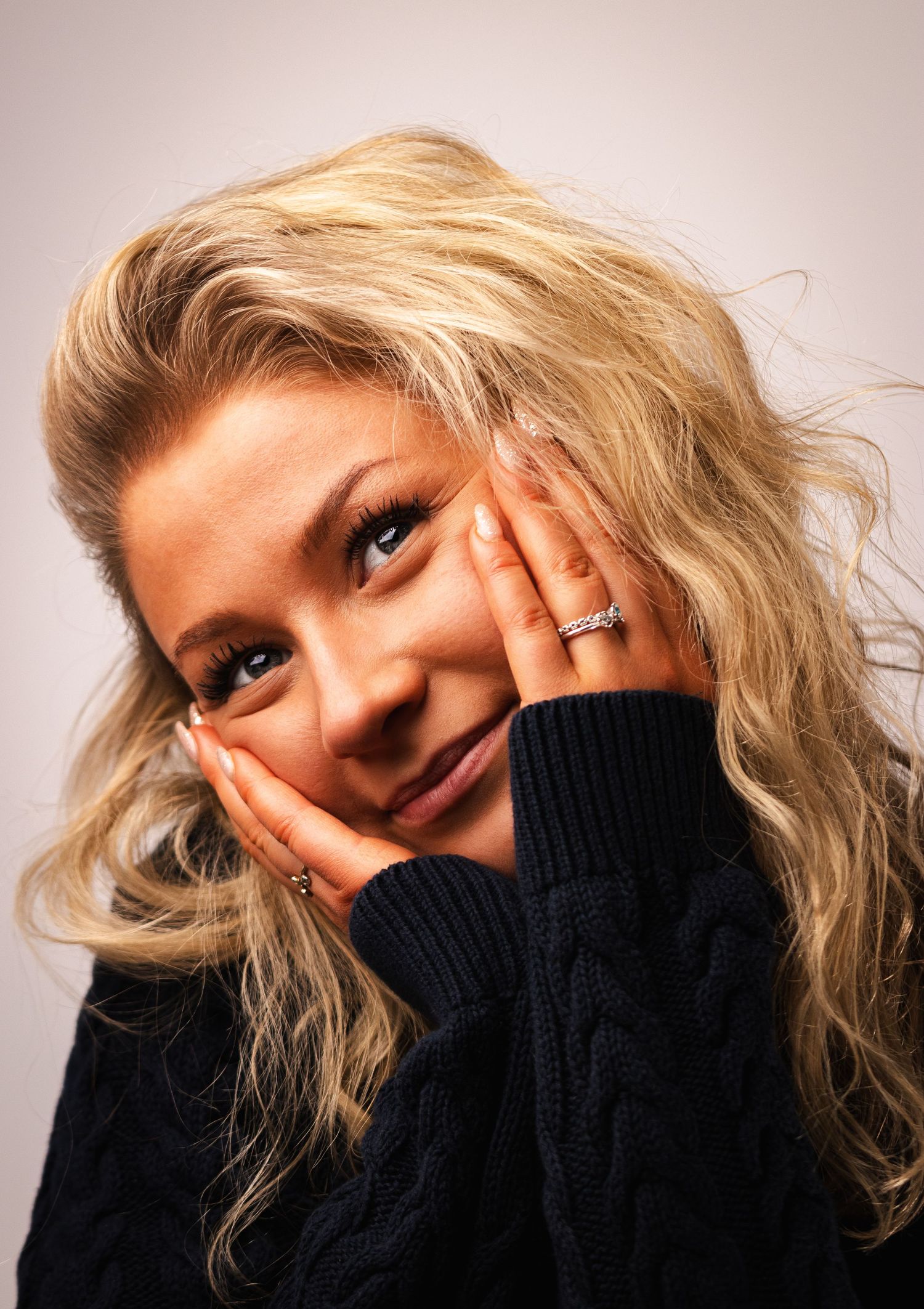 Portrait showcasing a sparkling engagement ring as someone poses with hands by their face.