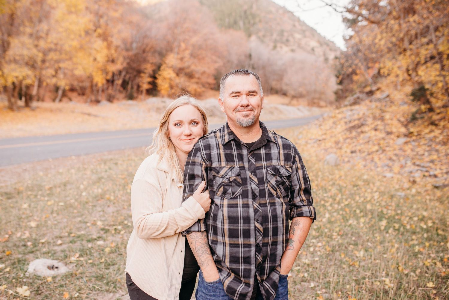 A couple poses together on a mountain road during golden autumn weather.