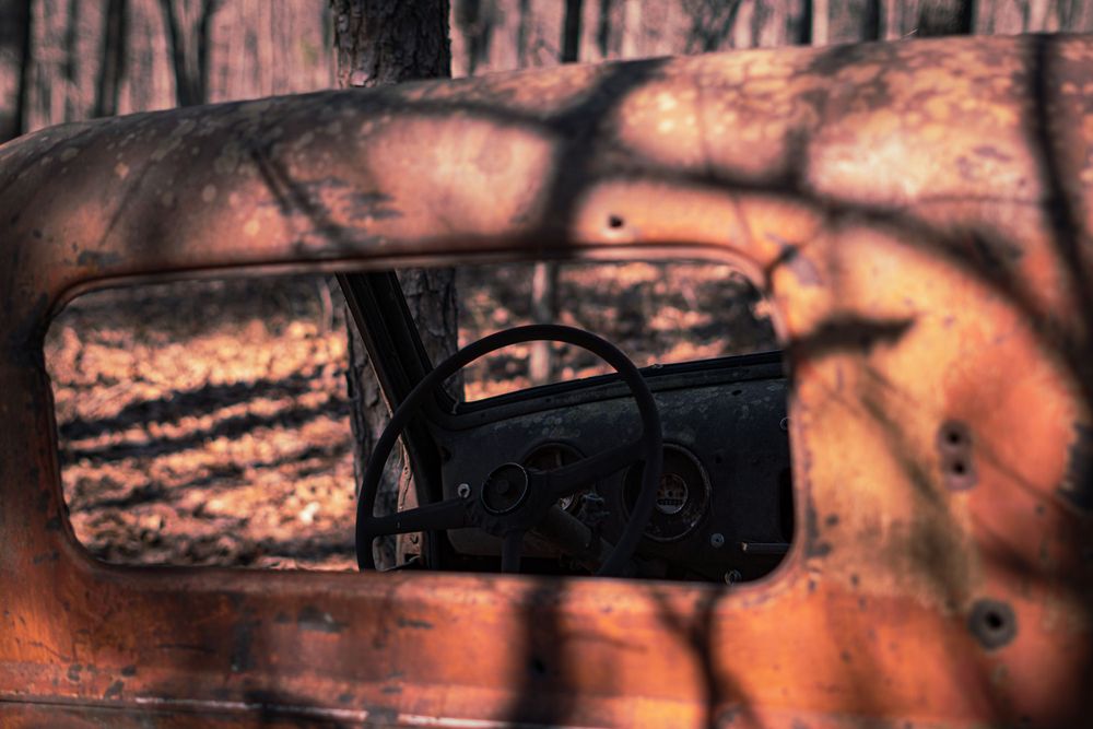 Close-up of rusted car rearview mirror with warm sunset lighting and tree shadows.