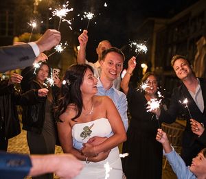 A couple embraces during their wedding celebration while guests hold sparklers around them at night.