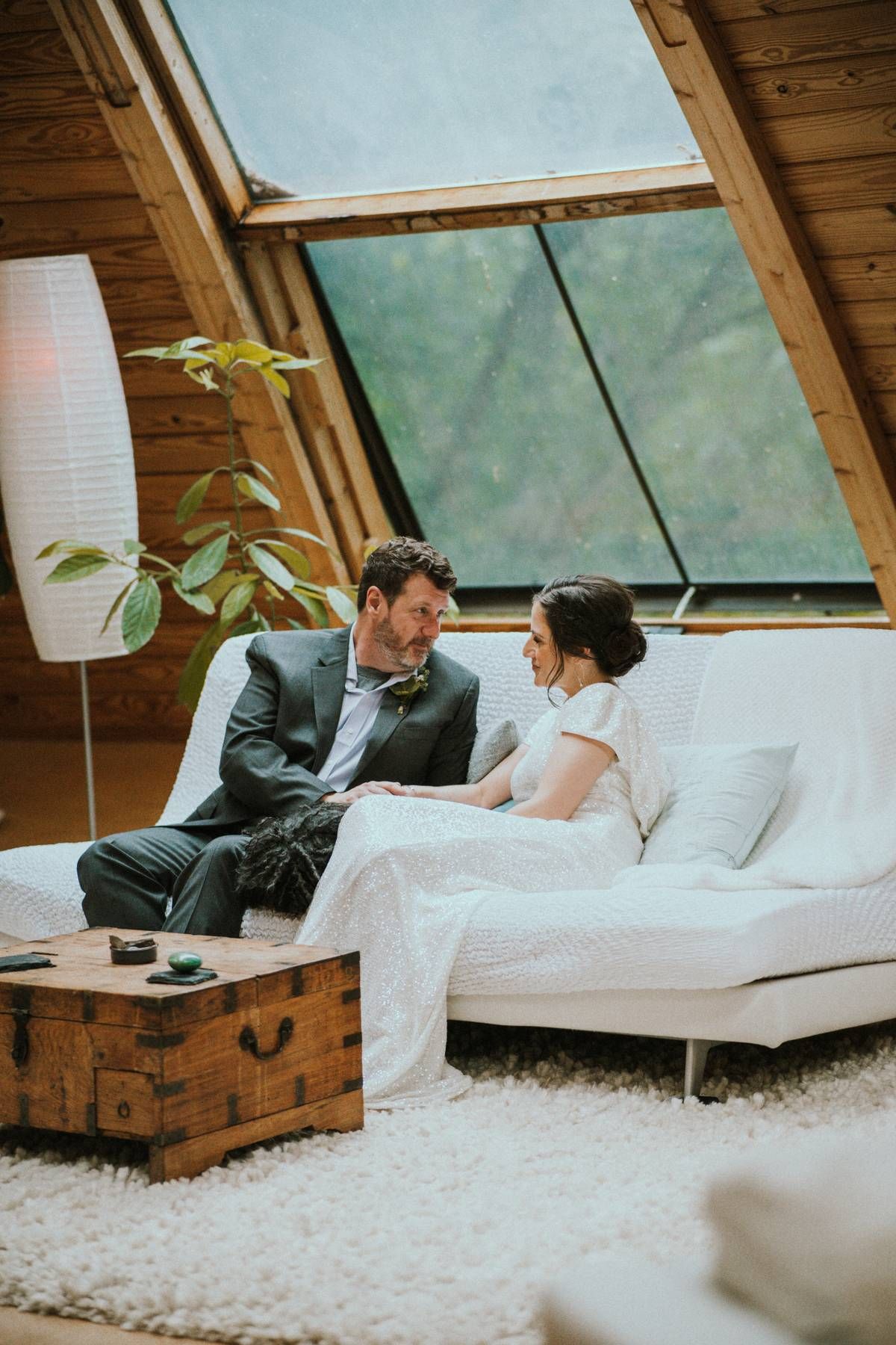 a bride and groom sitting on a white couch staring loving at each other as they talk on their wedding day