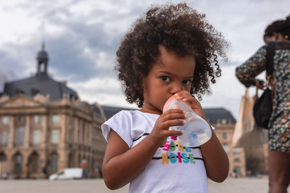 Young child in white t-shirt drinking from cup in front of historic European building.