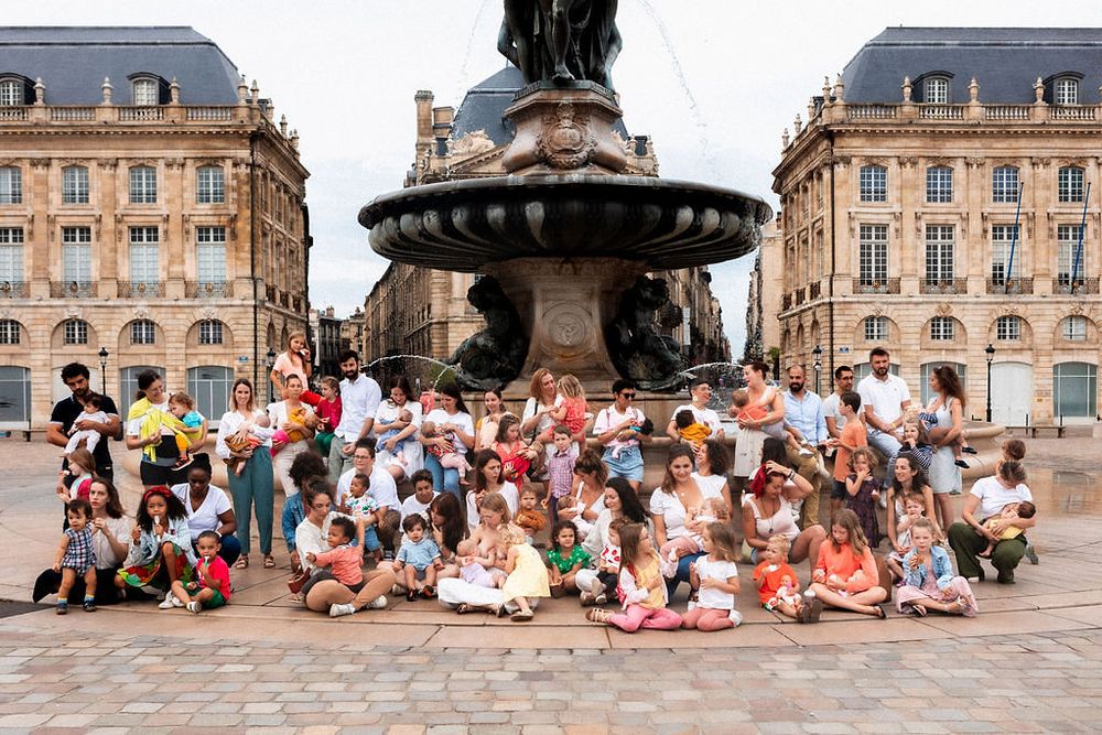 Large group photo of families gathered around a fountain in a historic European city square.
