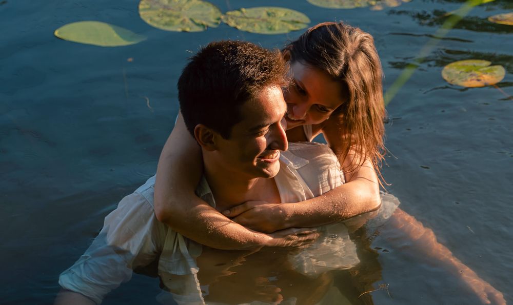 Couple embracing romantically in a serene lily pad pond, sharing a joyful moment in the water.