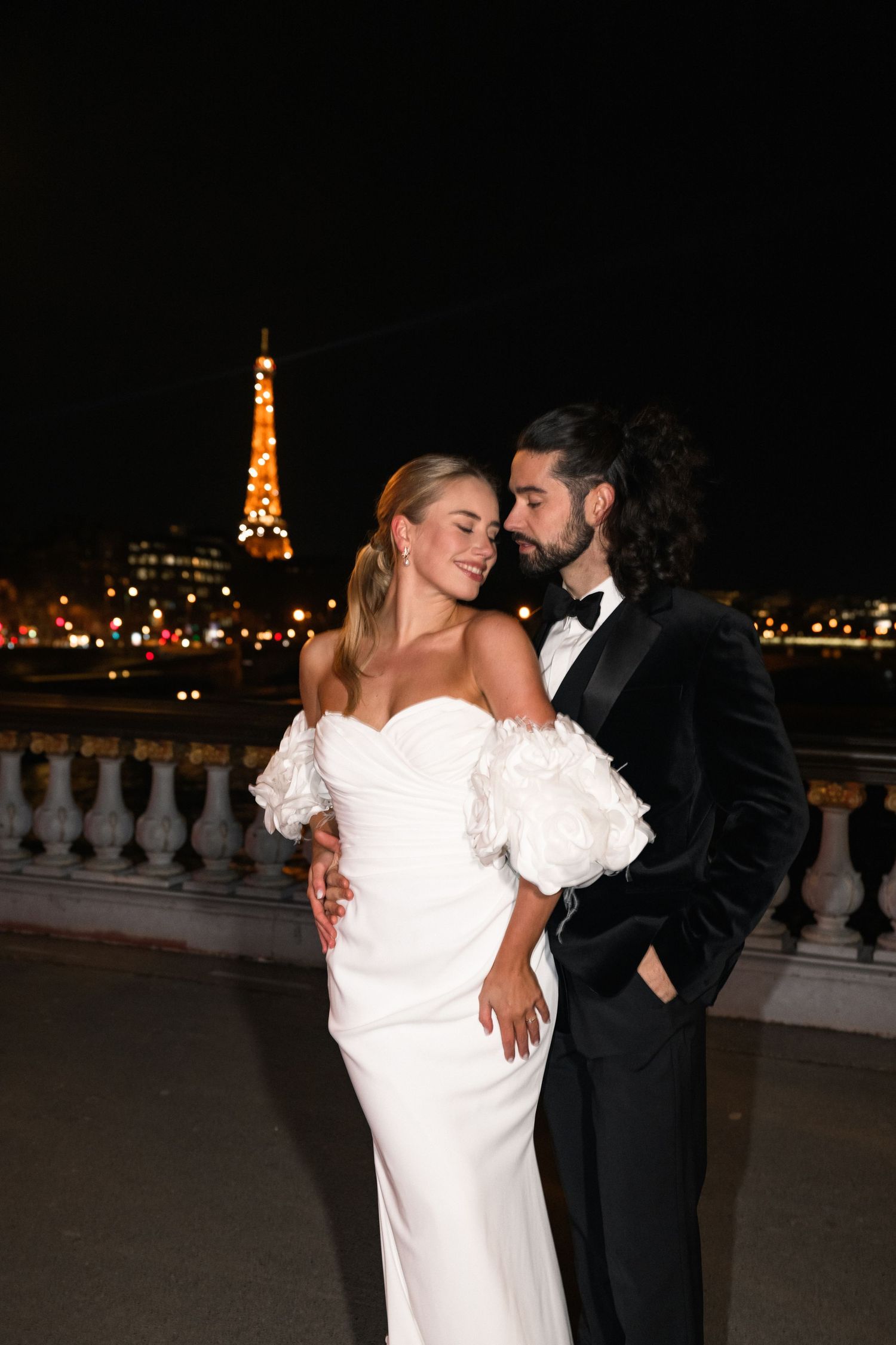 A romantic nighttime portrait in formalwear with the illuminated Eiffel Tower in the distance.