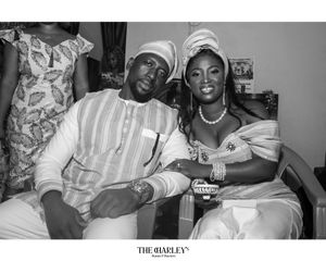 A black and white photograph showing two individuals wearing white traditional attire sitting together in a casual setting.