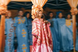 Traditional ceremony with person in pink dress and background attendants in blue.
