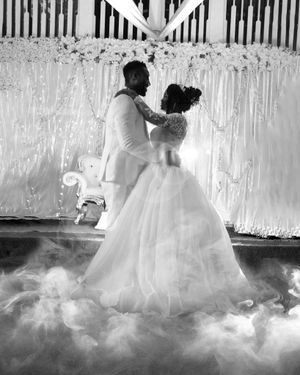A romantic wedding couple dances on a foggy dance floor under white drapery and twinkling lights in black and white.